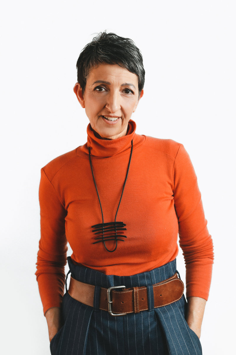 Mohi Skin Care founder Tracey Holland. Tracey is smiling, while looking directly at the camera. She is wearing a tangerine turtleneck with blue pinstripe pants.